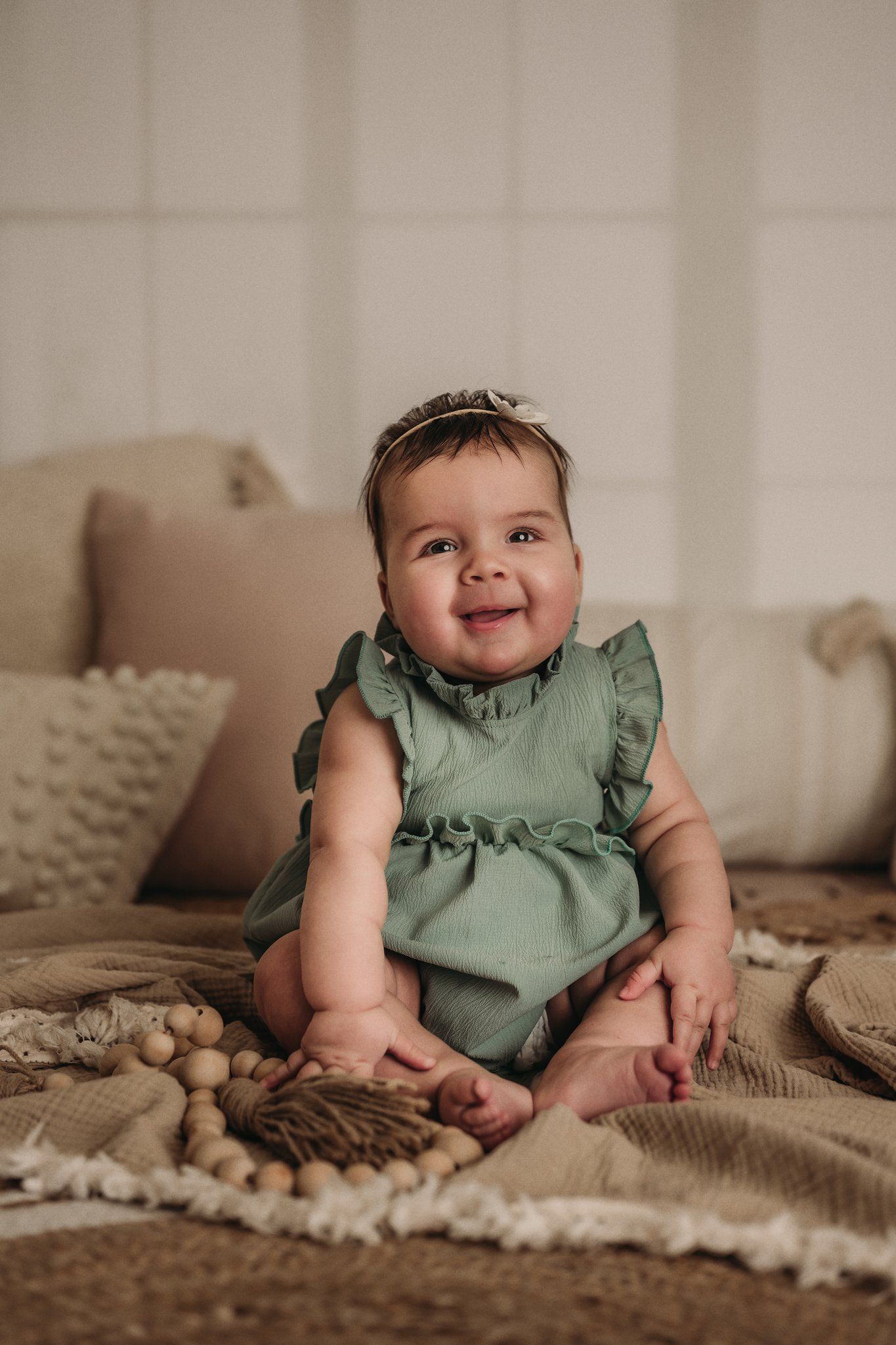A joyful baby in mint green dress sits on neutral textured blankets.