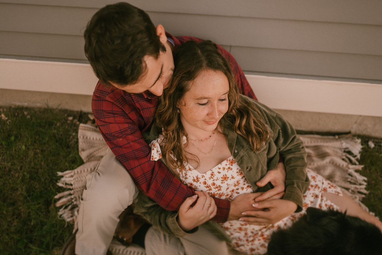 Romantic couple sharing tender moment on blanket by house in warm evening light.