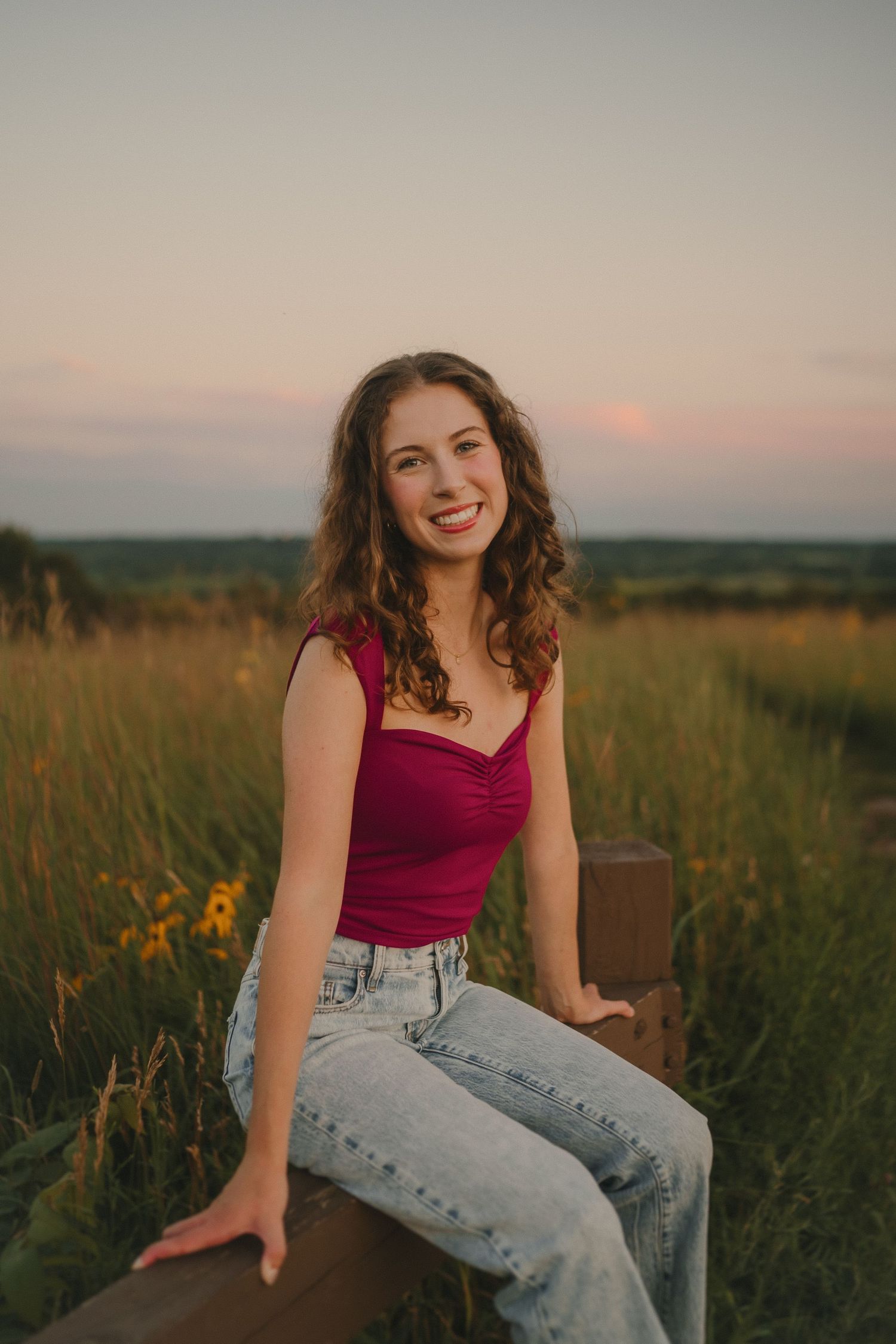 Someone in a red top and jeans sits casually on a wooden surface during golden hour.