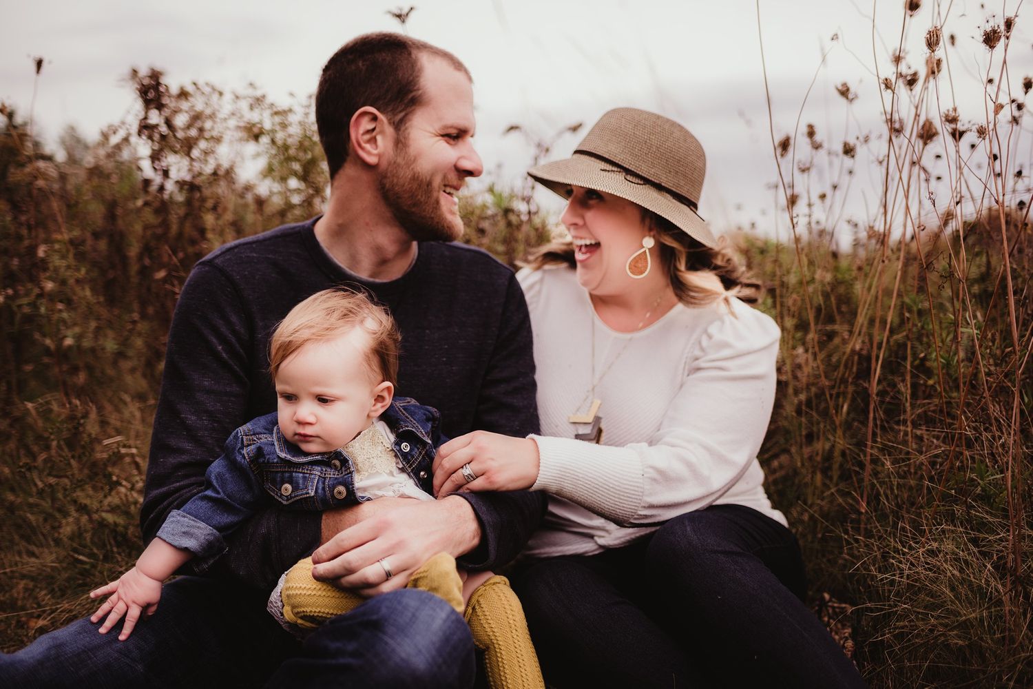 A family sharing a candid moment while sitting in tall grass during autumn.