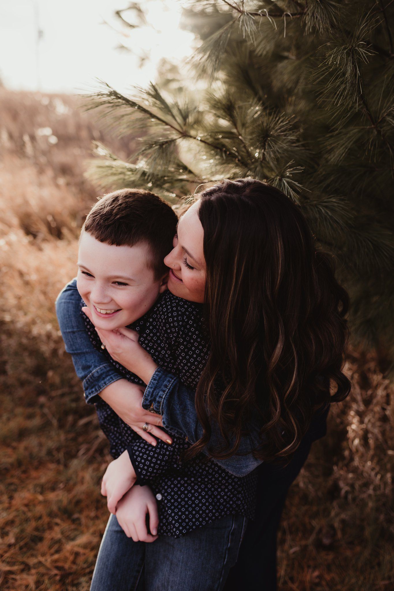 A playful embrace between two people against a background of pine trees.