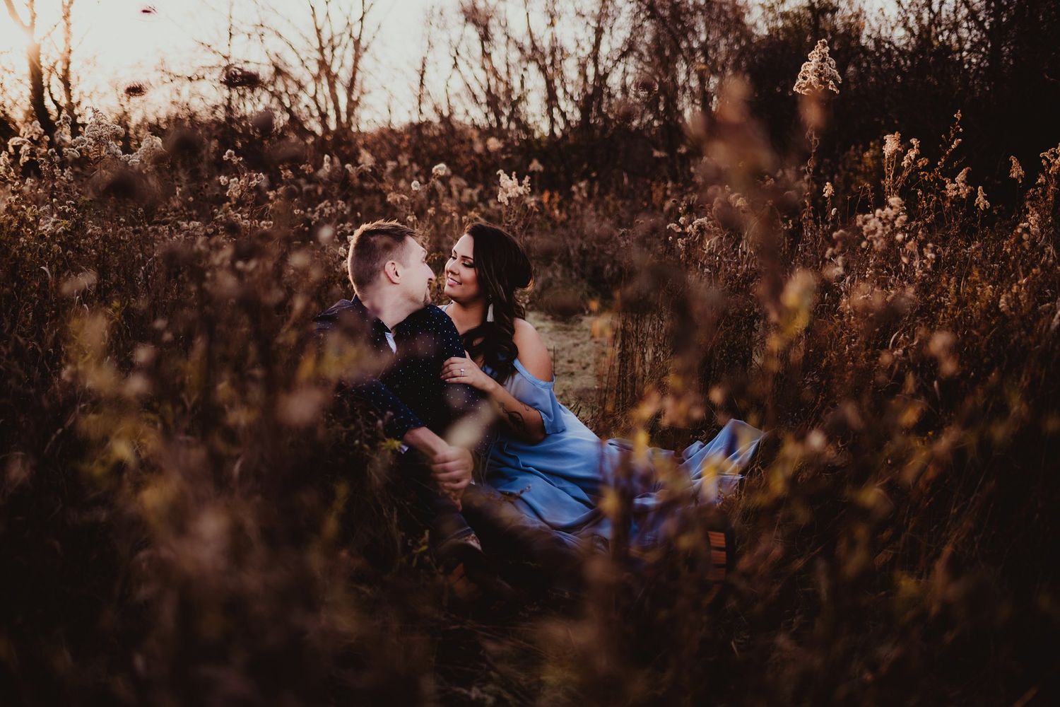 Romantic sunset portrait of couple sitting among tall grasses in autumn field.