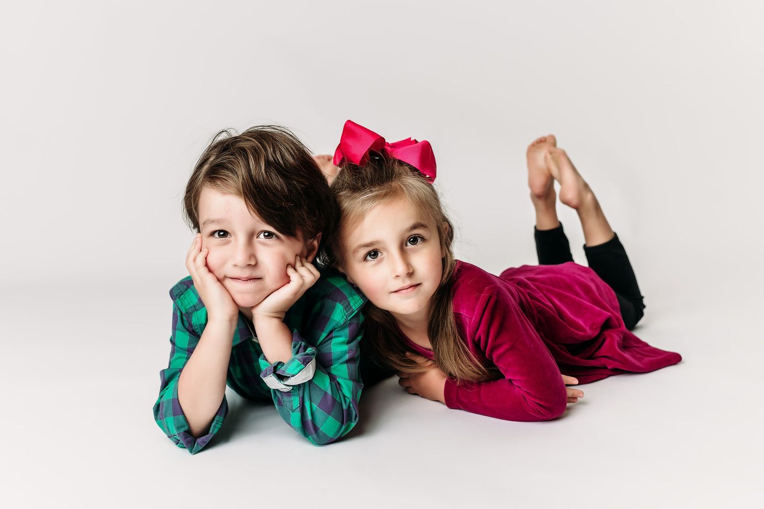 Children in green plaid and burgundy velvet pose playfully on white backdrop.