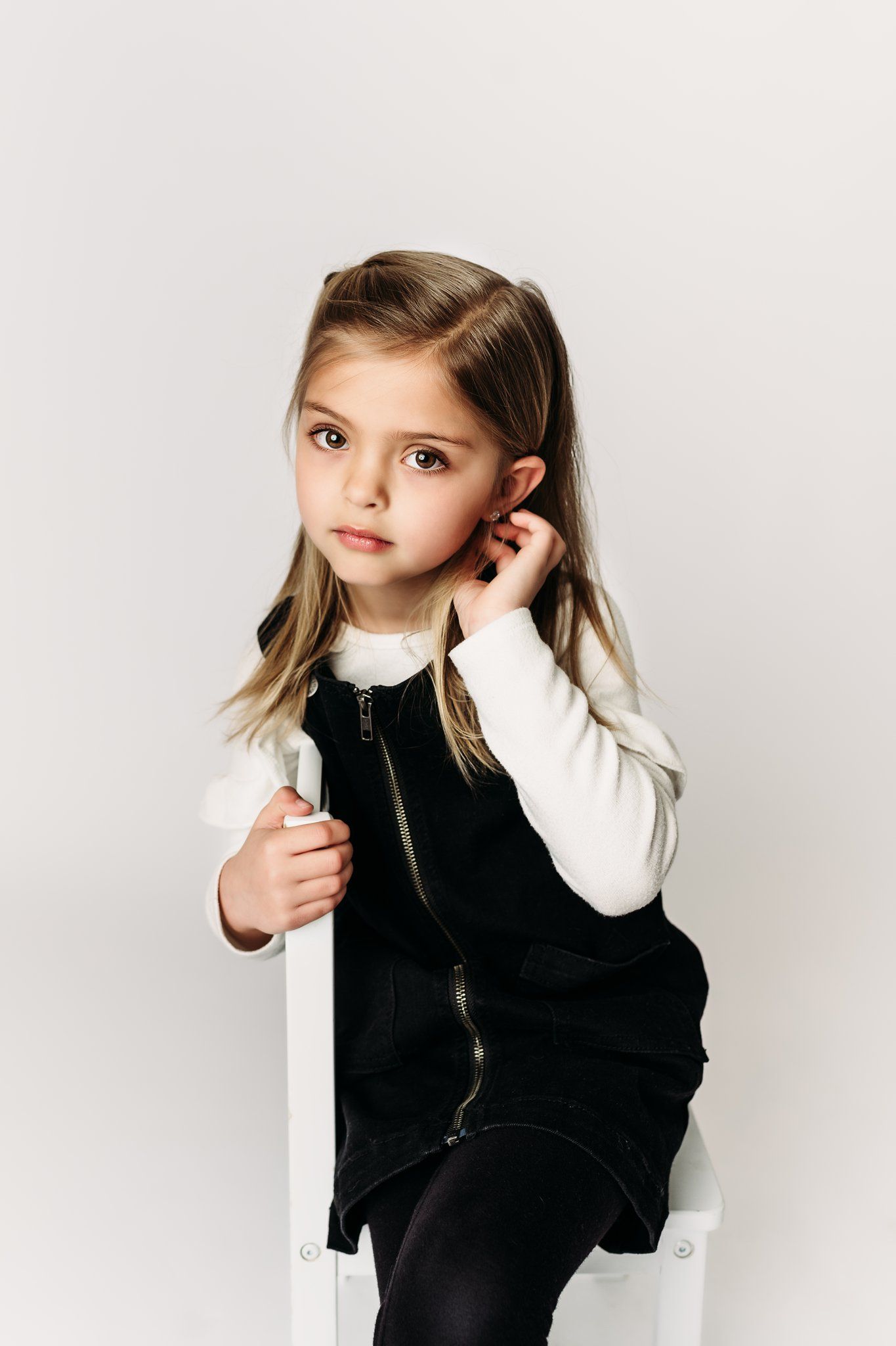 A child in a black pinafore dress and white shirt poses against a white background.