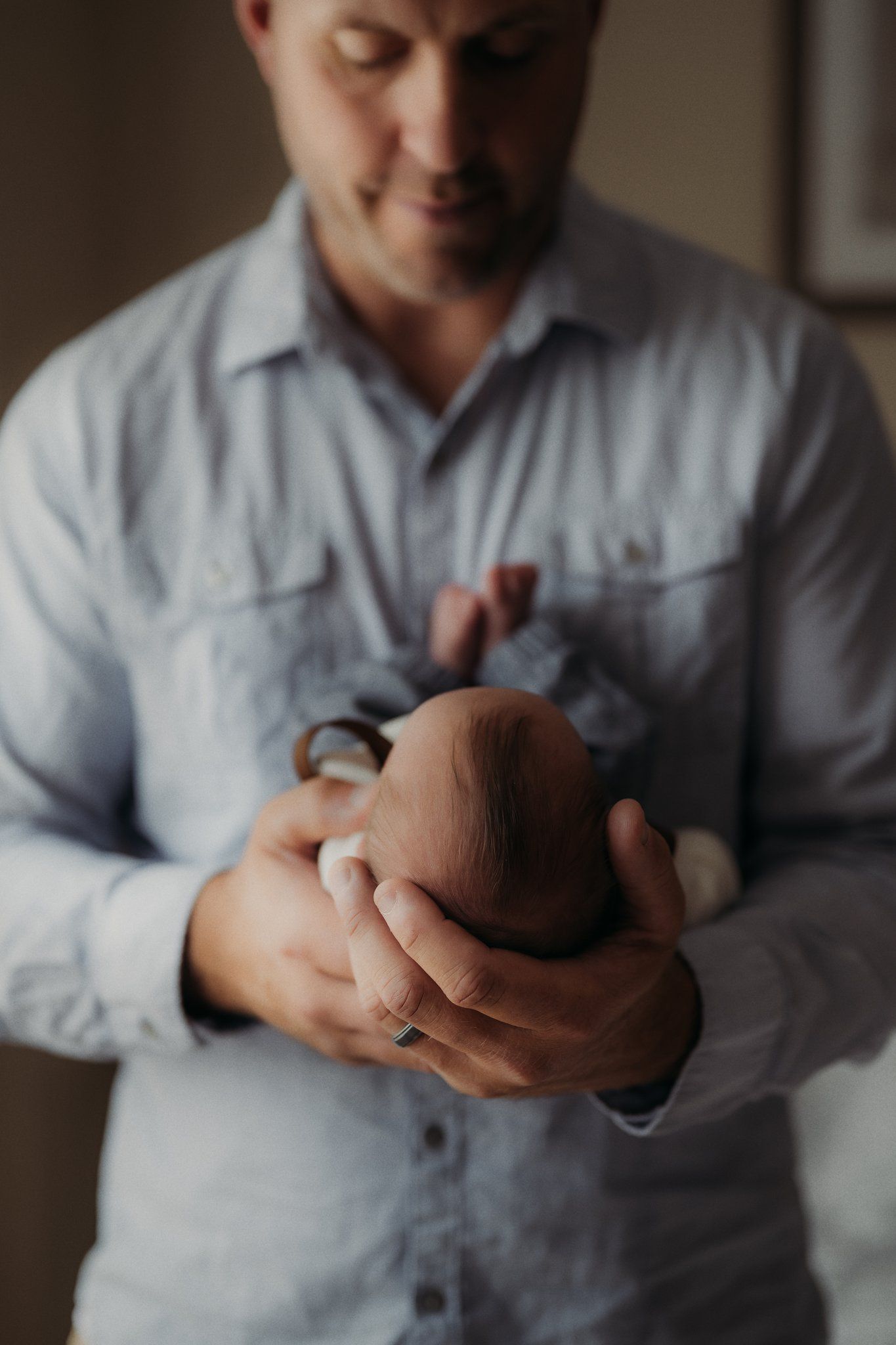 Parent in blue button-down shirt gently holds sleeping newborn baby.