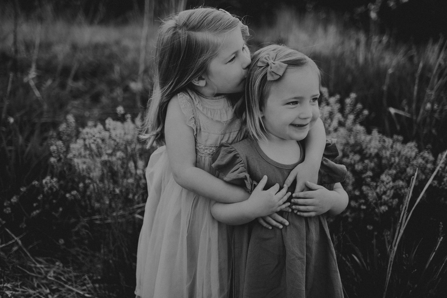 Black and white portrait of two children sharing a joyful embrace outdoors.