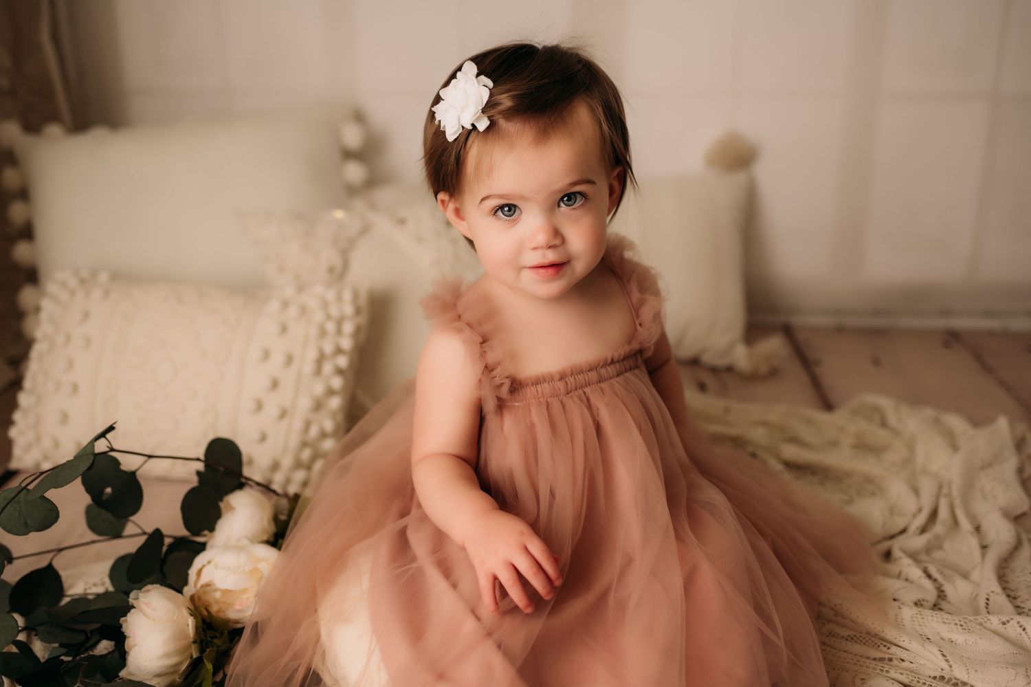 Baby in pink tulle dress sits on cream blanket with roses for portrait session.