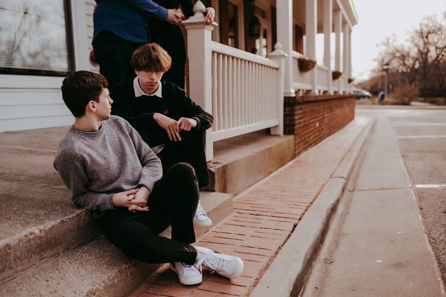 Two people sit casually on steps having a conversation outside a building.