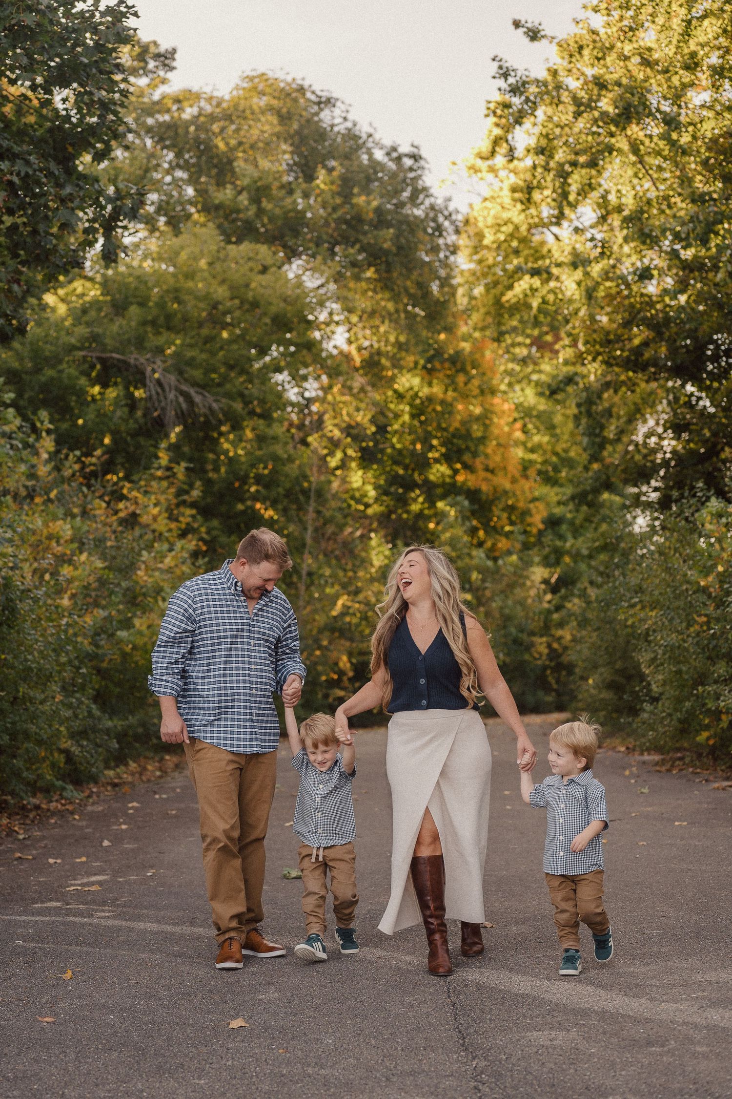 A family walks together on a path surrounded by golden autumn trees during sunset.