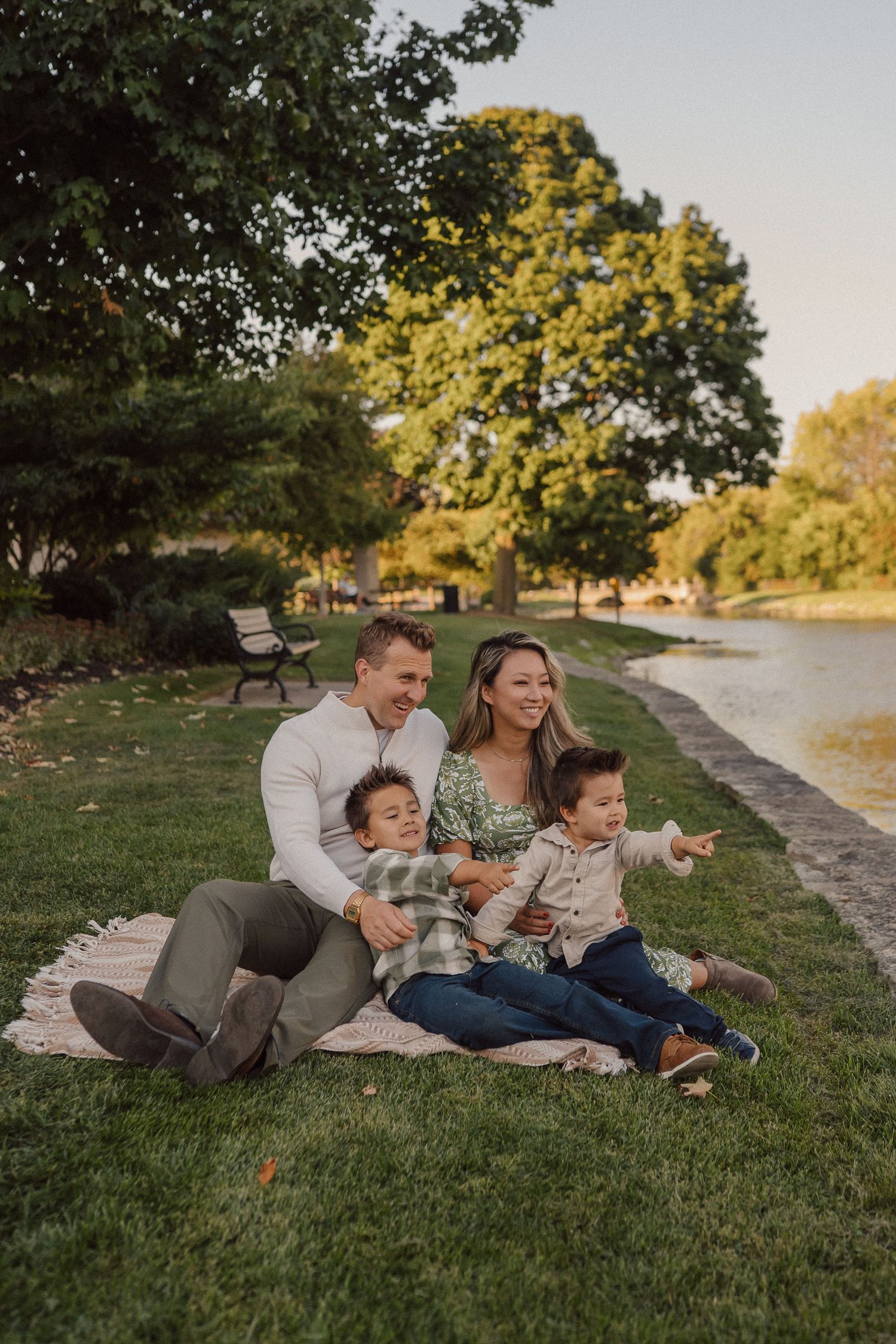 Family enjoying playful moments together on grassy riverbank during golden hour sunset.