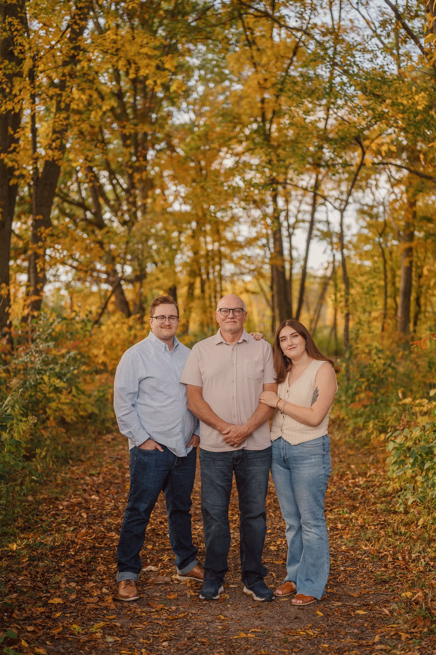 A family poses together in an autumn forest setting with golden leaves and warm lighting.