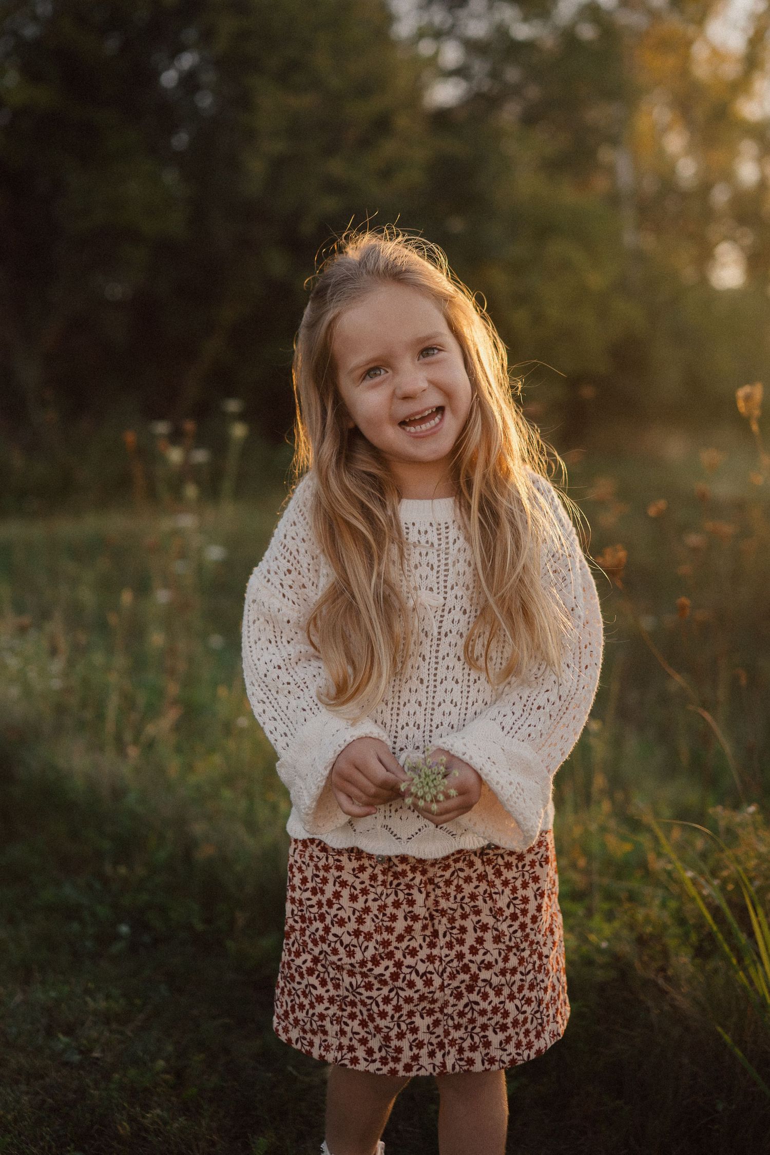 Girl in white knit sweater laughs joyfully during sunset outdoor portrait session.