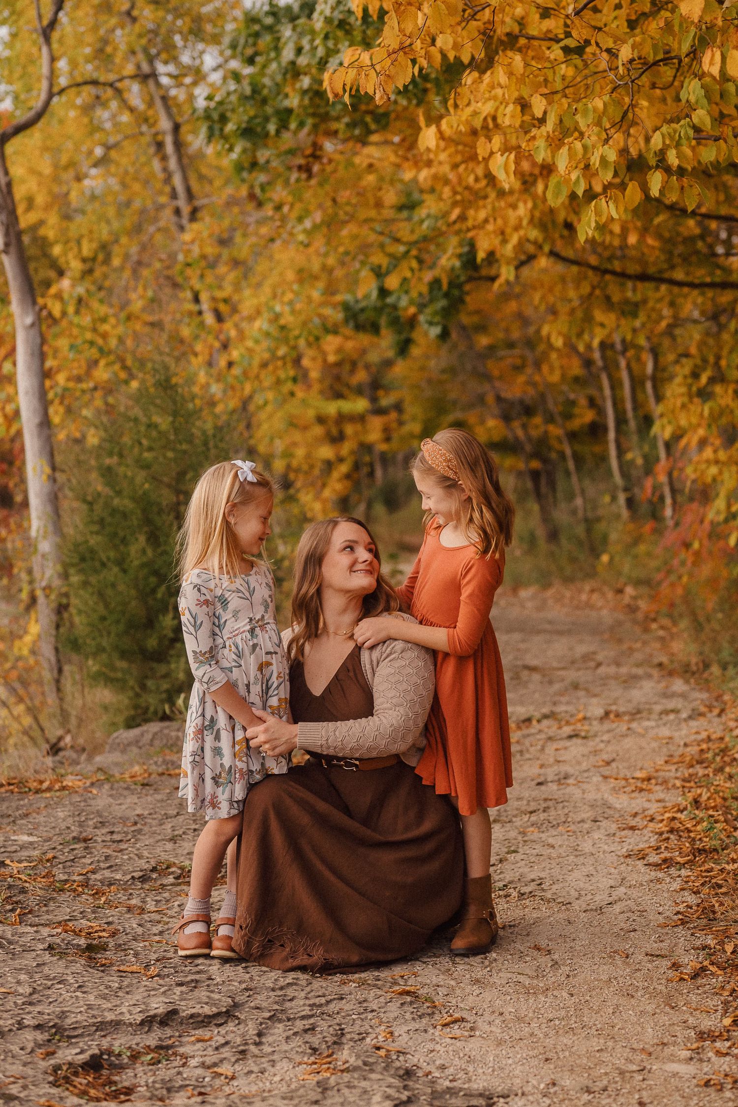 Tender family moment captured on autumn trail with golden leaves in background.