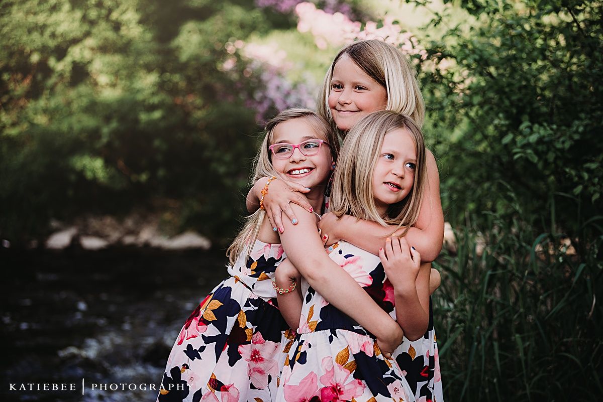 Three people share warm embrace while posing in garden with blooming flowers.