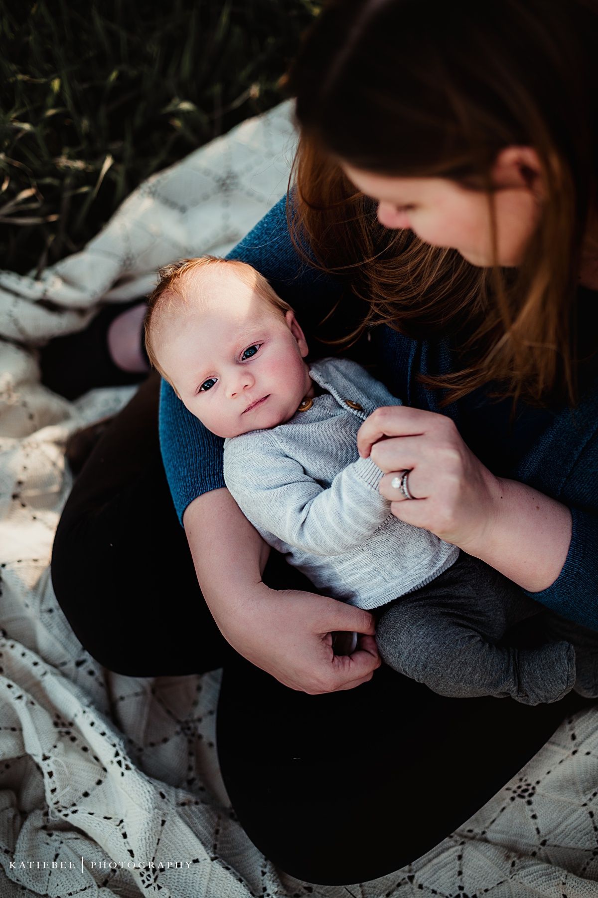 Intimate lifestyle portrait showing gentle interaction between parent and infant on white blanket.