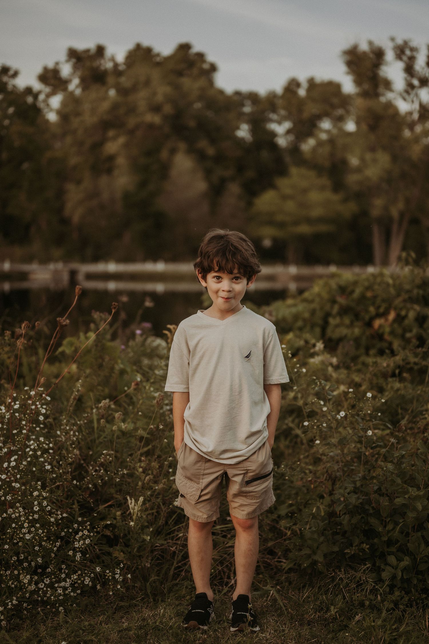 A child stands in tall grass and wildflowers at sunset wearing a light colored t-shirt and khaki shorts.