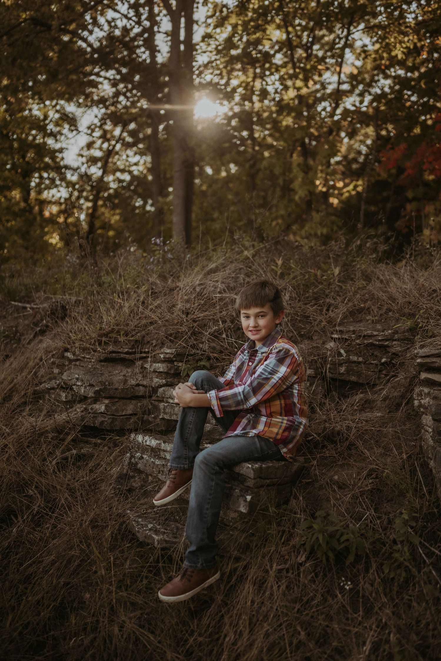 Young person sitting on fallen logs in a wooded area during sunset.