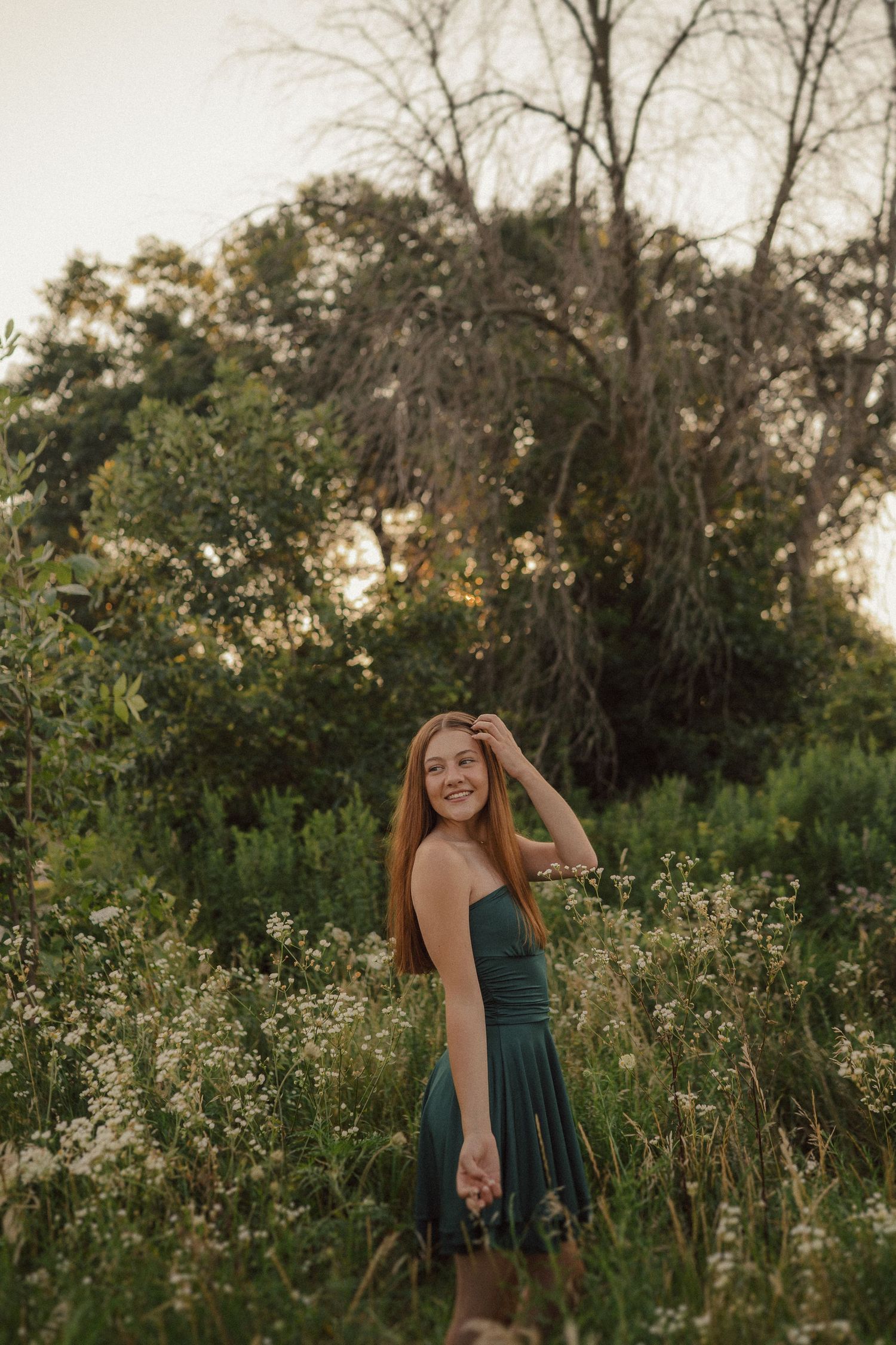 Person spins playfully in emerald dress amidst a field of white wildflowers at dusk.