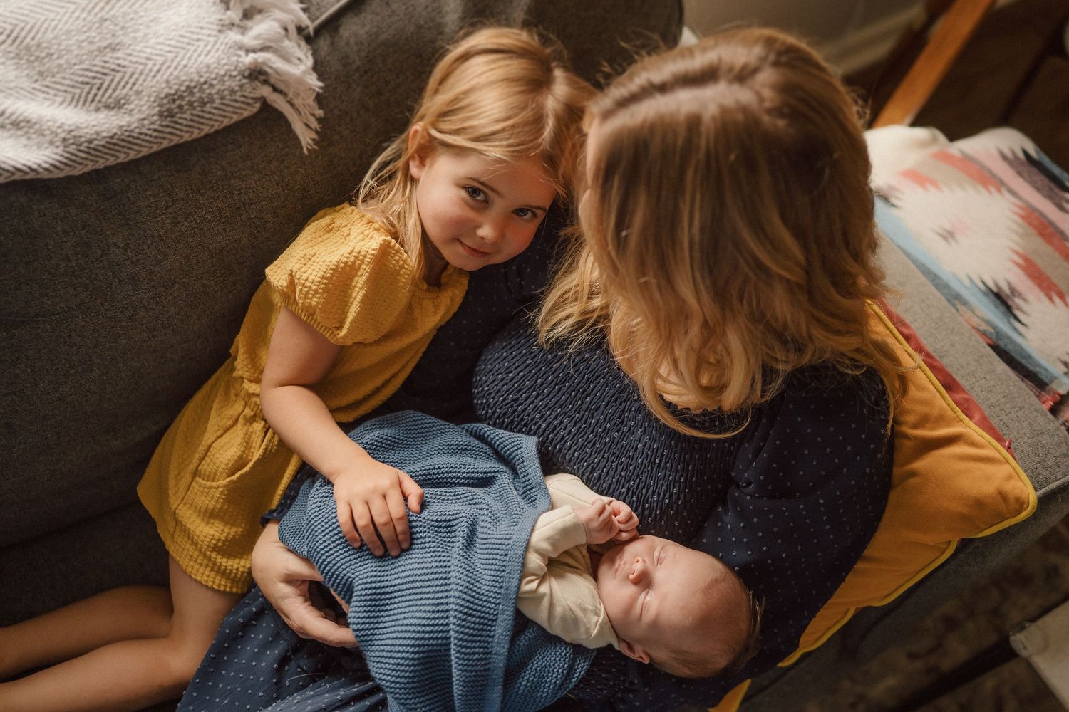 A tender family moment captured on a dark couch with yellow and blue tones.