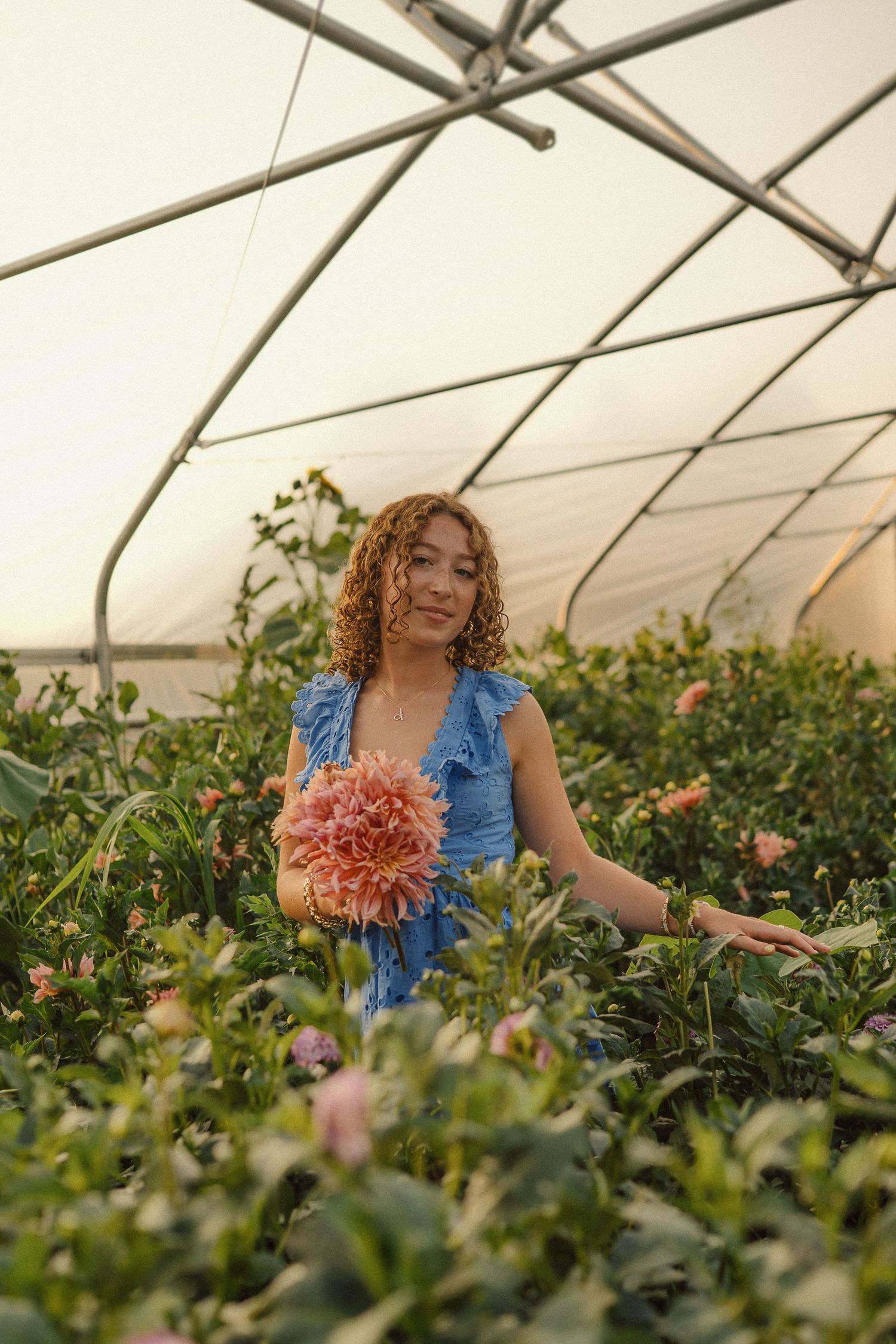 A bright blue romper stands out among blooming flowers in a greenhouse setting.