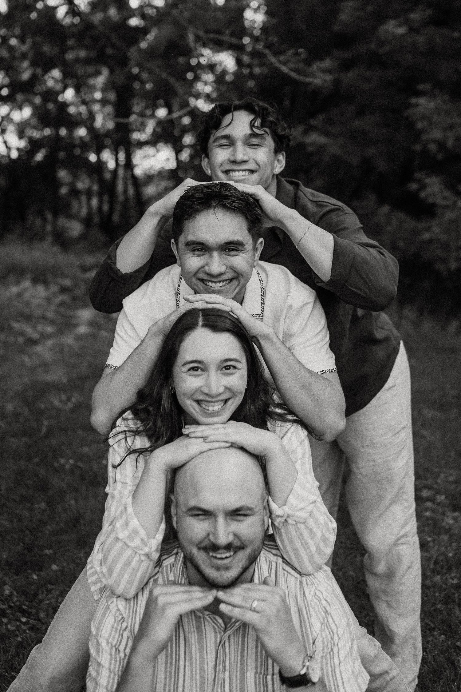 Black and white photo of four siblings stacking heads in a playful outdoor portrait.