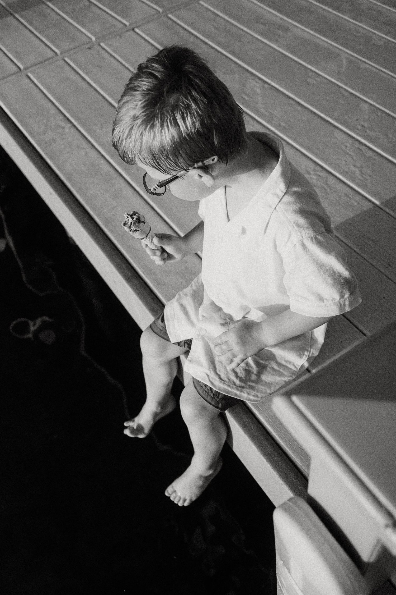 A young boy in glasses sits on a dock edge, holding a pinwheel toy.