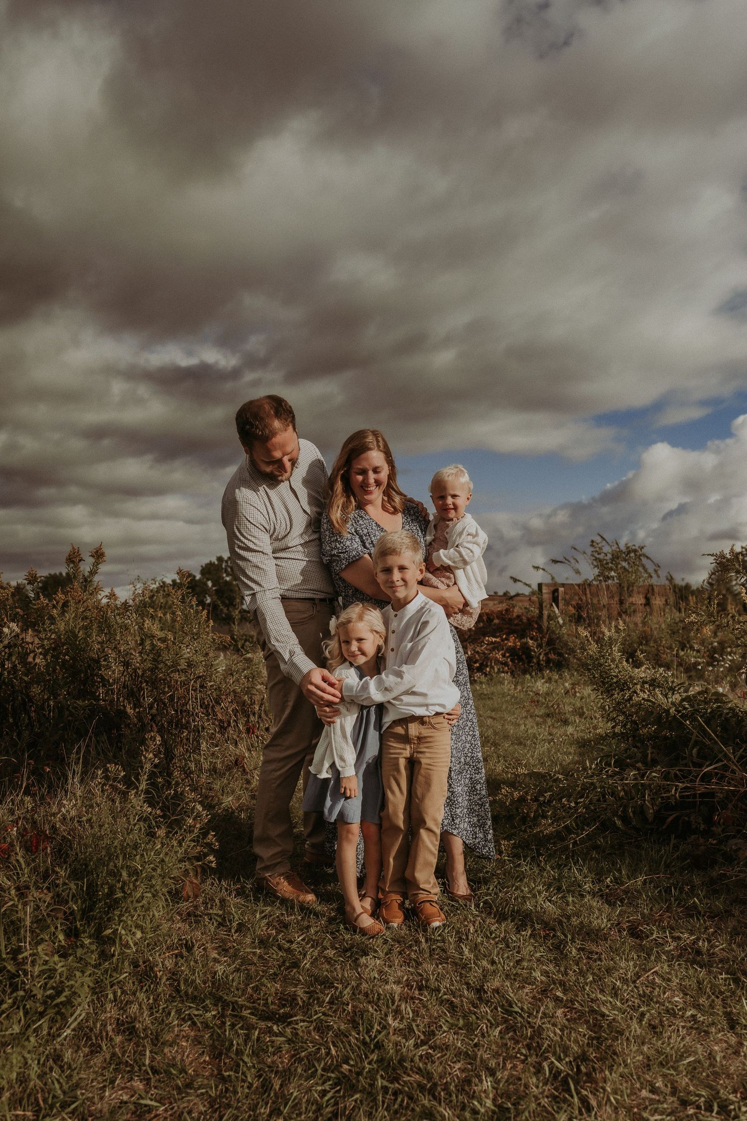 Warm family portrait in casual attire against moody autumn skies and wild grass.