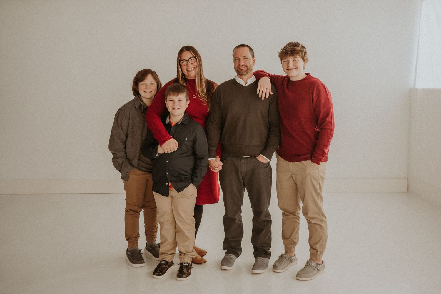 Family group of six poses together in earth tones against white studio backdrop.