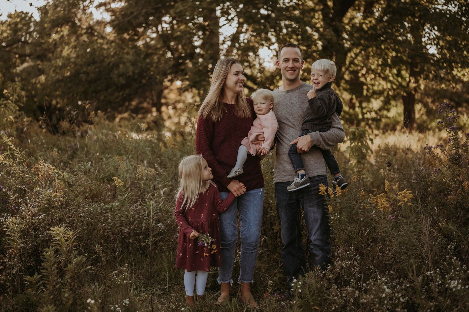 Casual family portrait against natural backdrop of trees and wild grass during sunset.