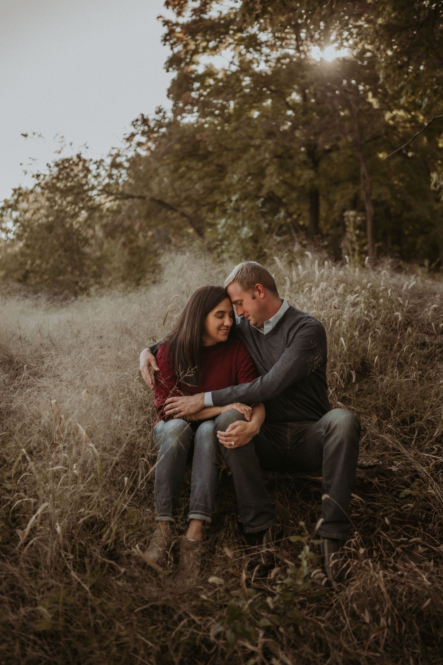 A couple shares an intimate moment while sitting together in tall autumn grass during sunset.