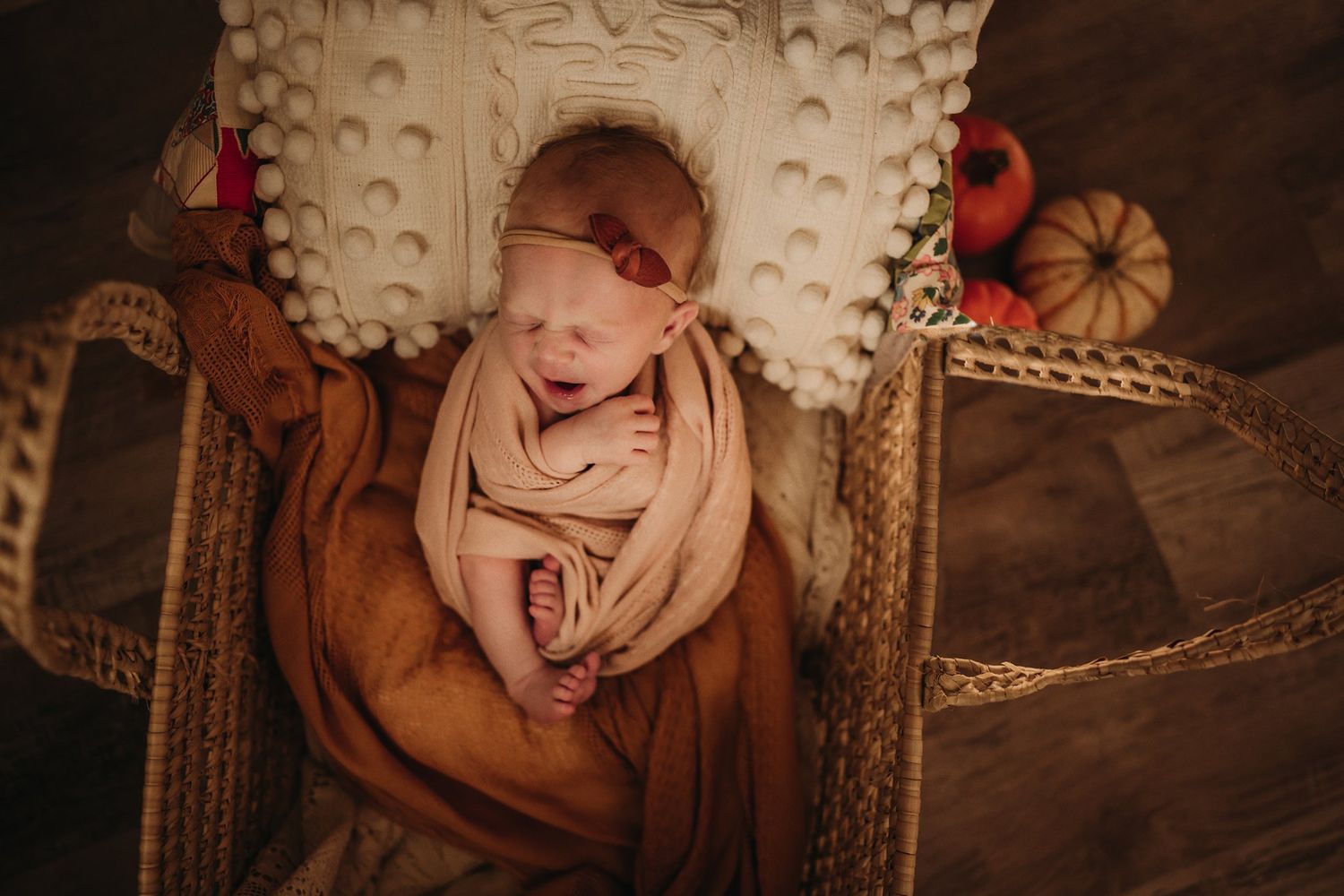Cozy autumn-themed newborn portrait with pumpkins and wicker decorations.
