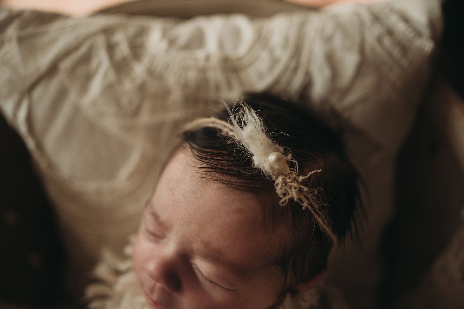 Close-up of sleeping baby with feathered headband against cream bedding.