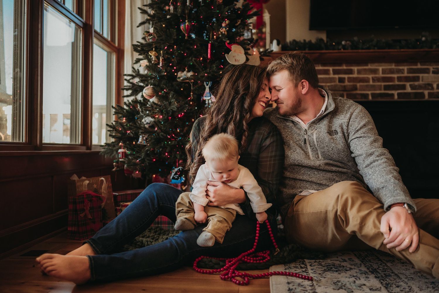 Cozy holiday scene by a Christmas tree with red beads and exposed brick fireplace.