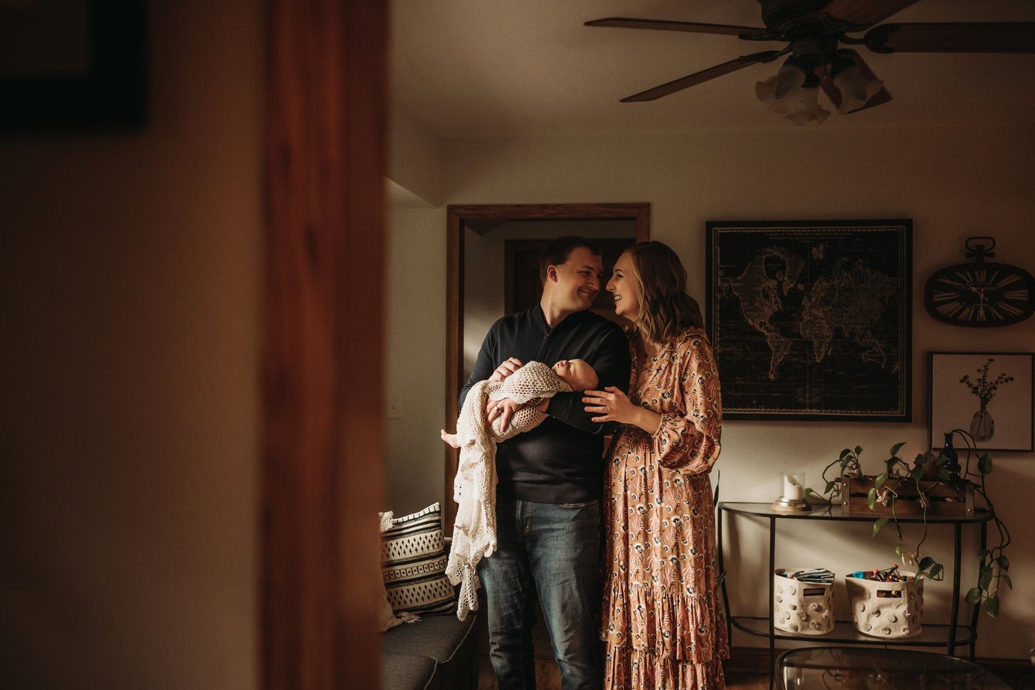 A warm family moment in a cozy living room as parents hold their swaddled newborn.