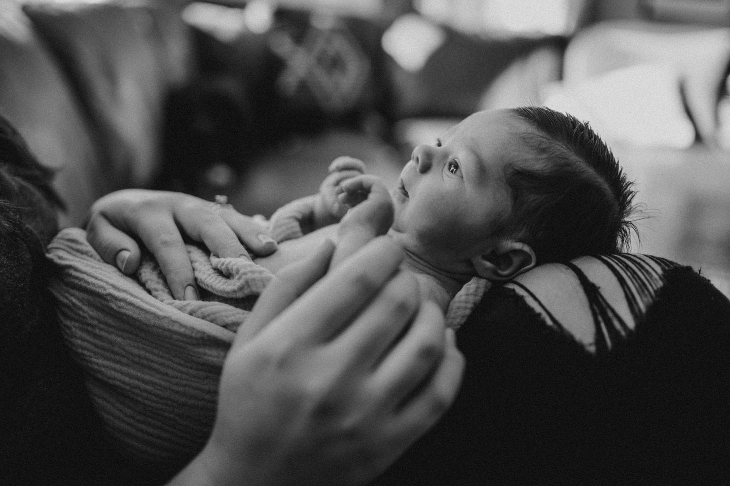 Black and white portrait of newborn baby being held against striped pillow.