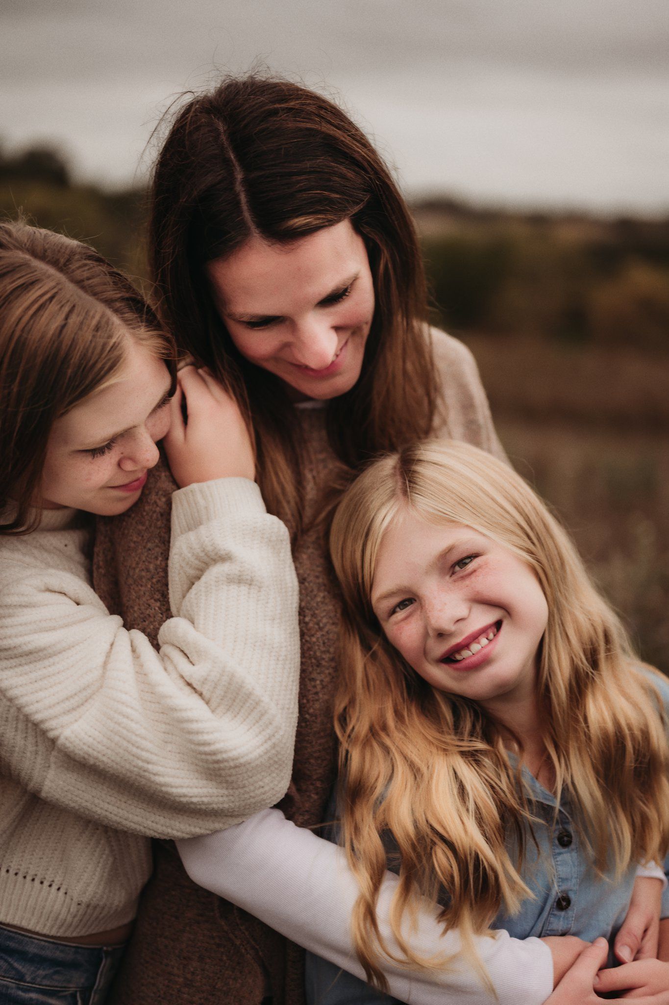 Candid moment of three people laughing and hugging together outdoors.