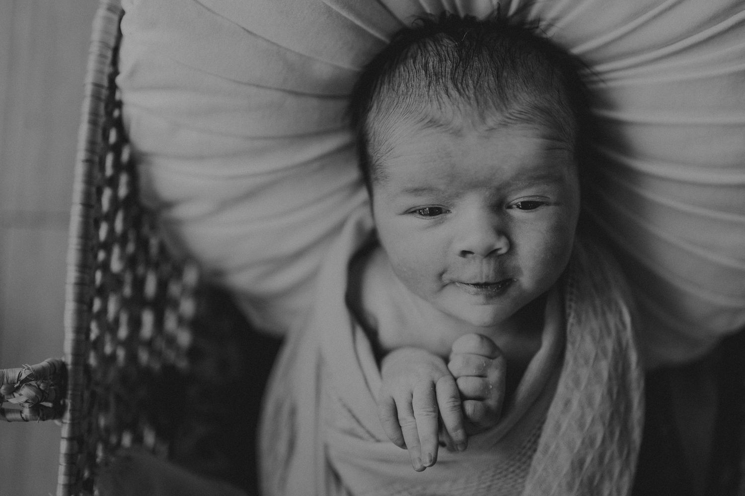 Black and white portrait of newborn baby wrapped in light fabric.