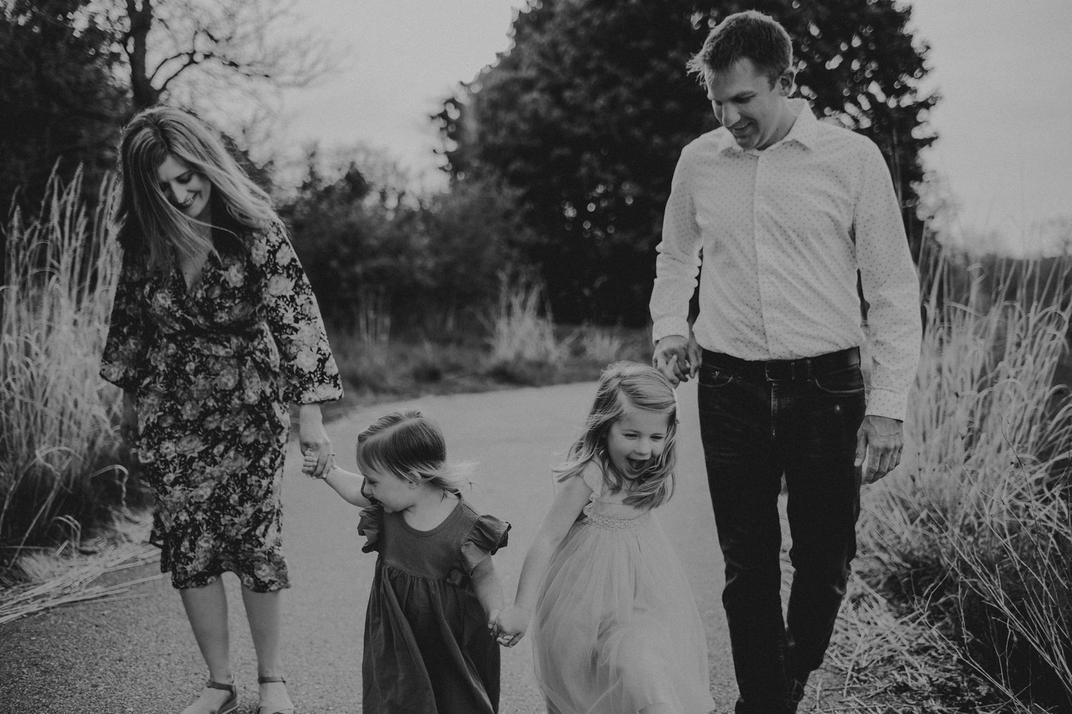 A black and white photo of a family walking together on a winding path surrounded by tall grass.
