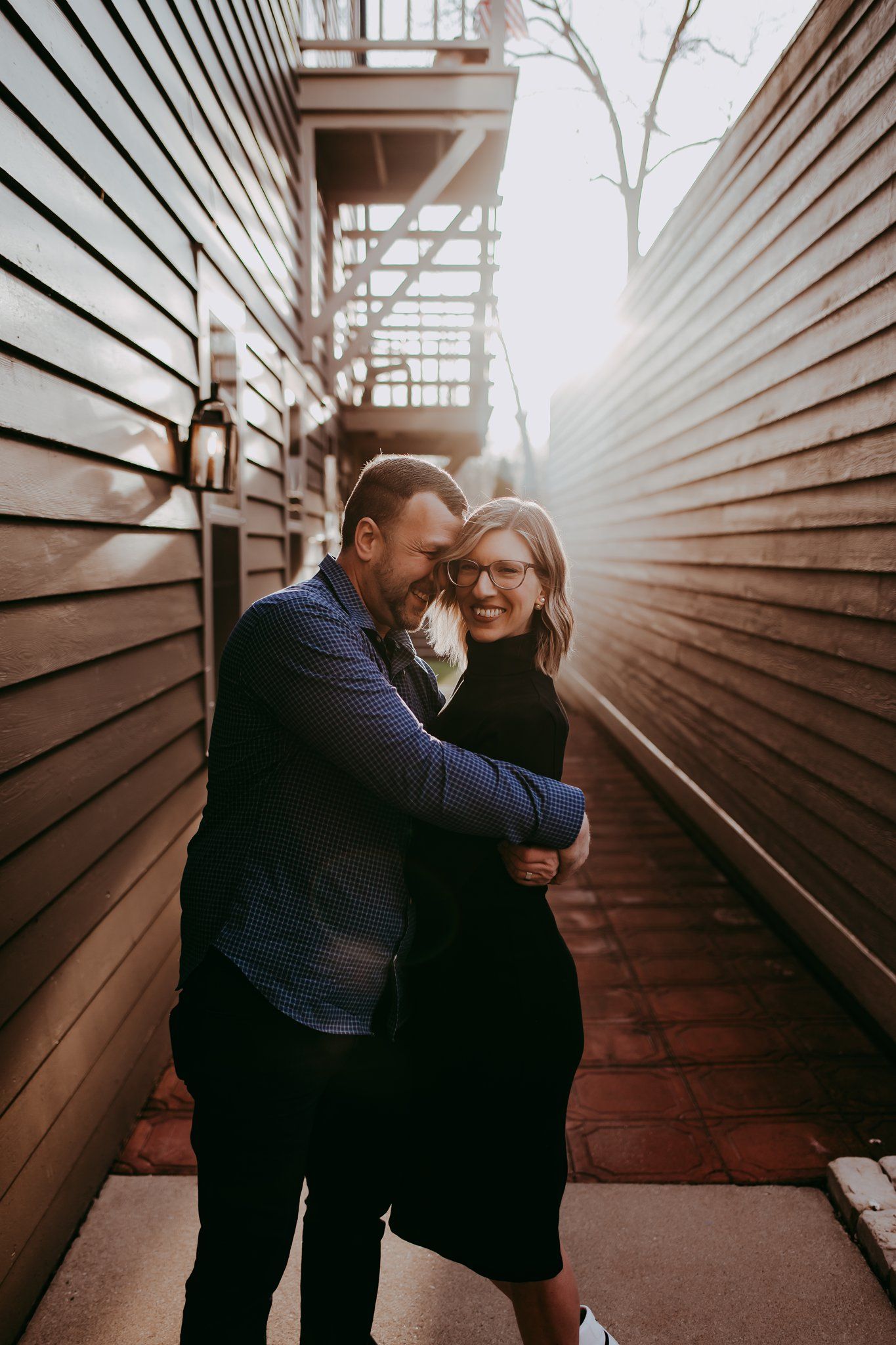 Intimate moment shared between couple laughing in narrow alleyway with wooden siding.