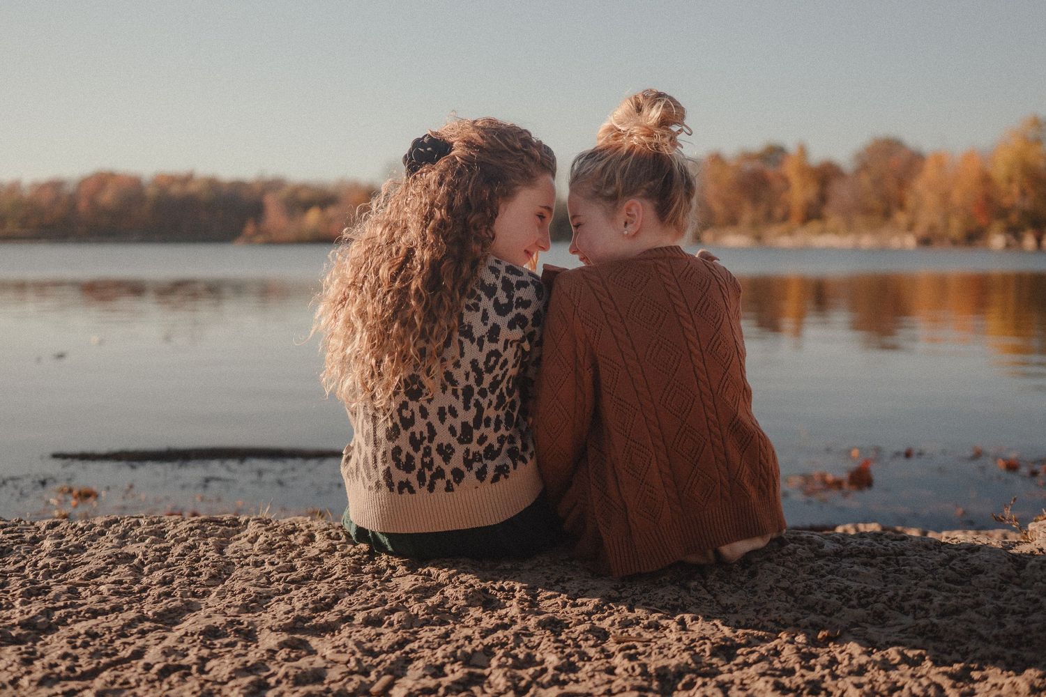Couple sitting by a lake during sunset with autumn foliage reflecting in the calm water.