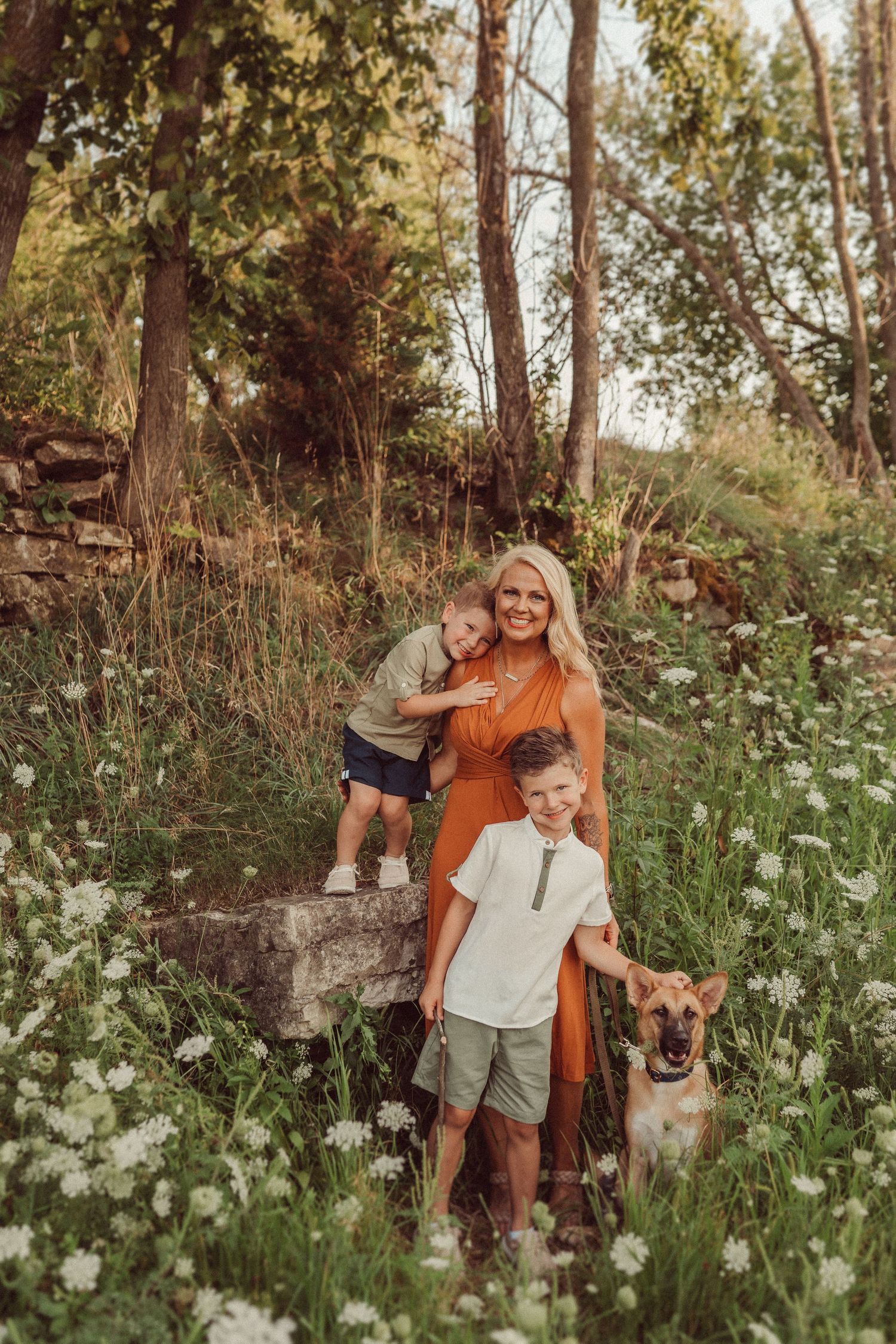 A family poses together with their German Shepherd dog among wildflowers and trees.