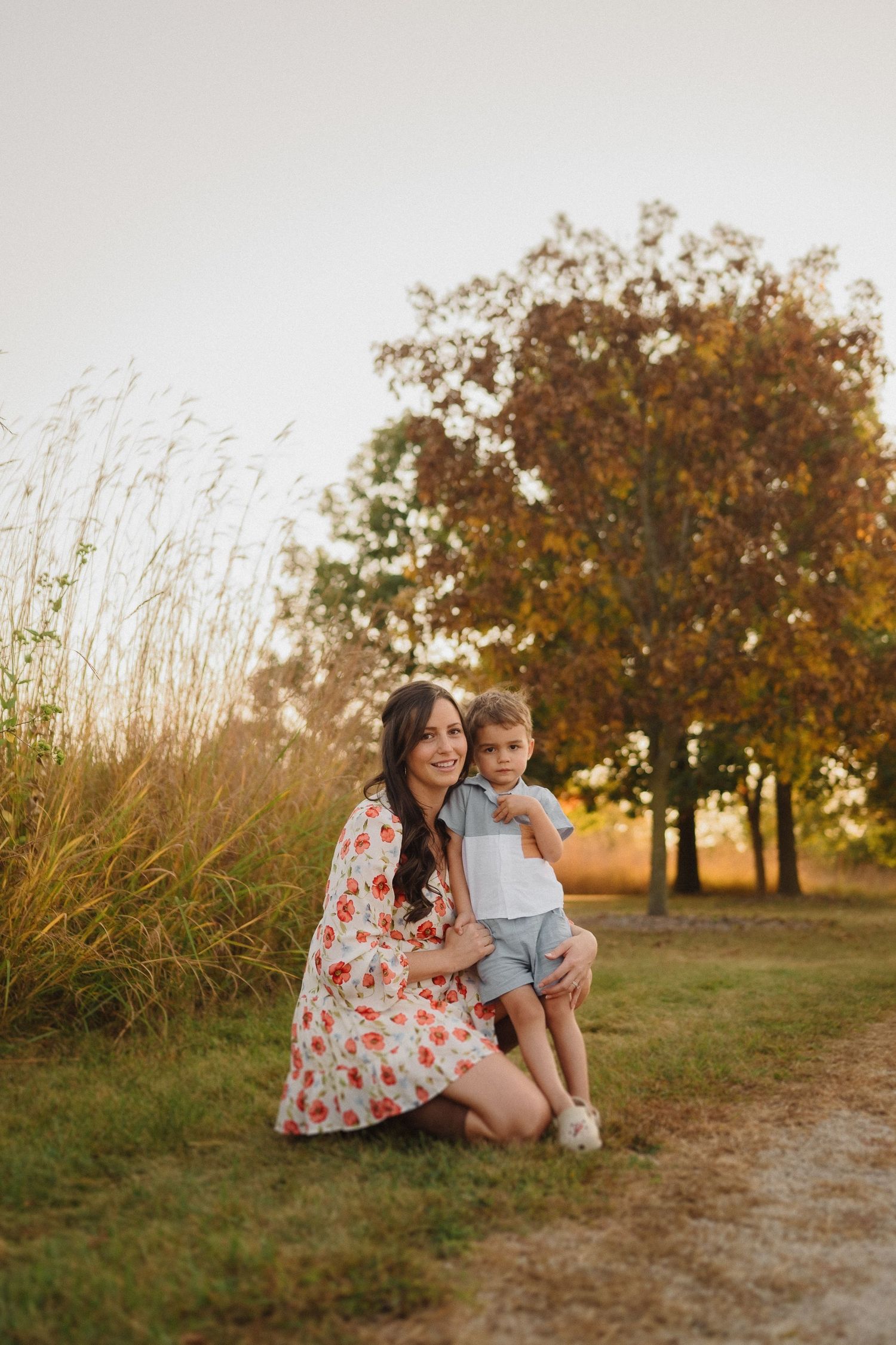 A warm sunset portrait of two people kneeling together on a path near tall grass.