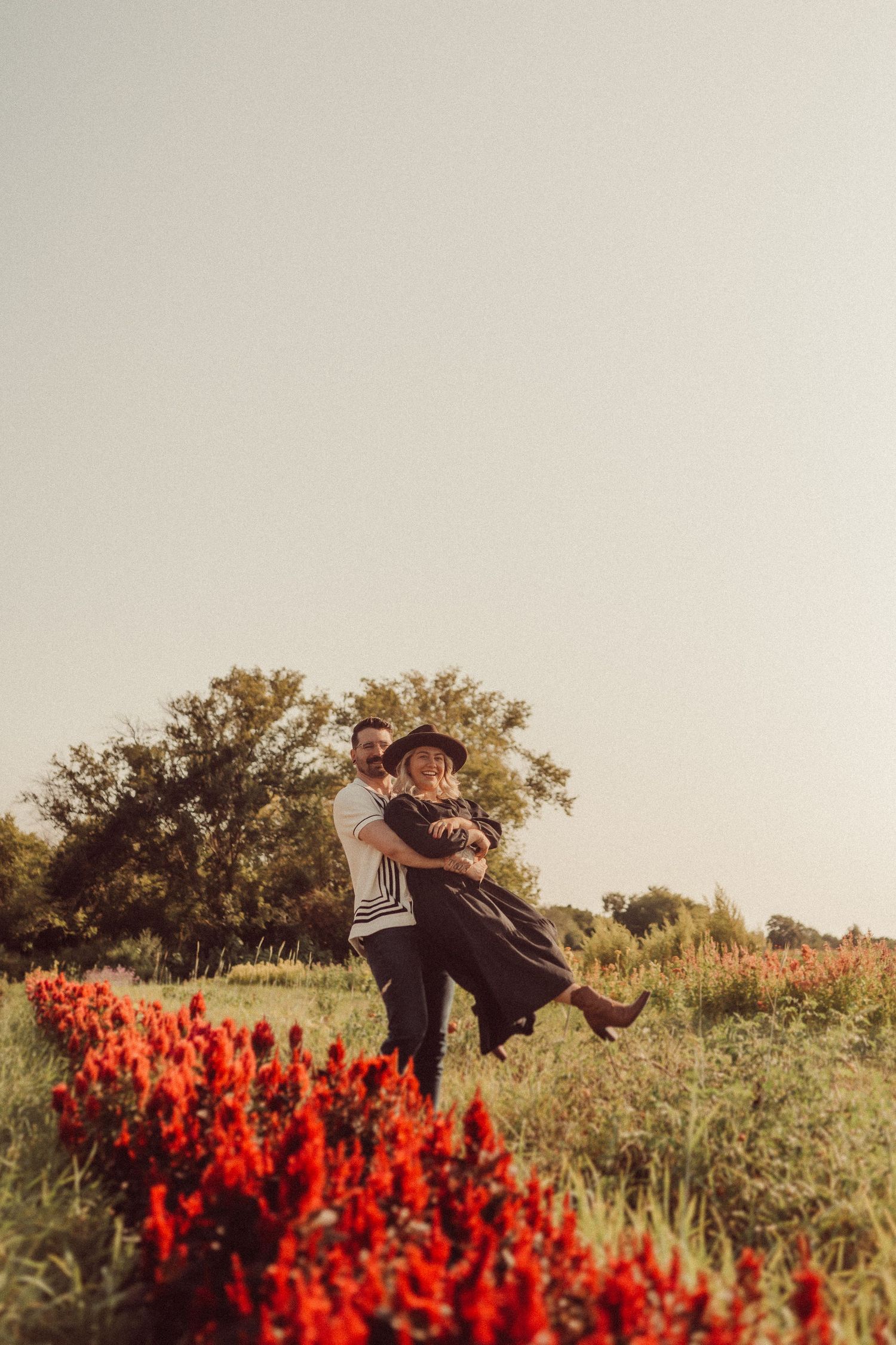 A playful moment captured as a couple spins in a field of red flowers.