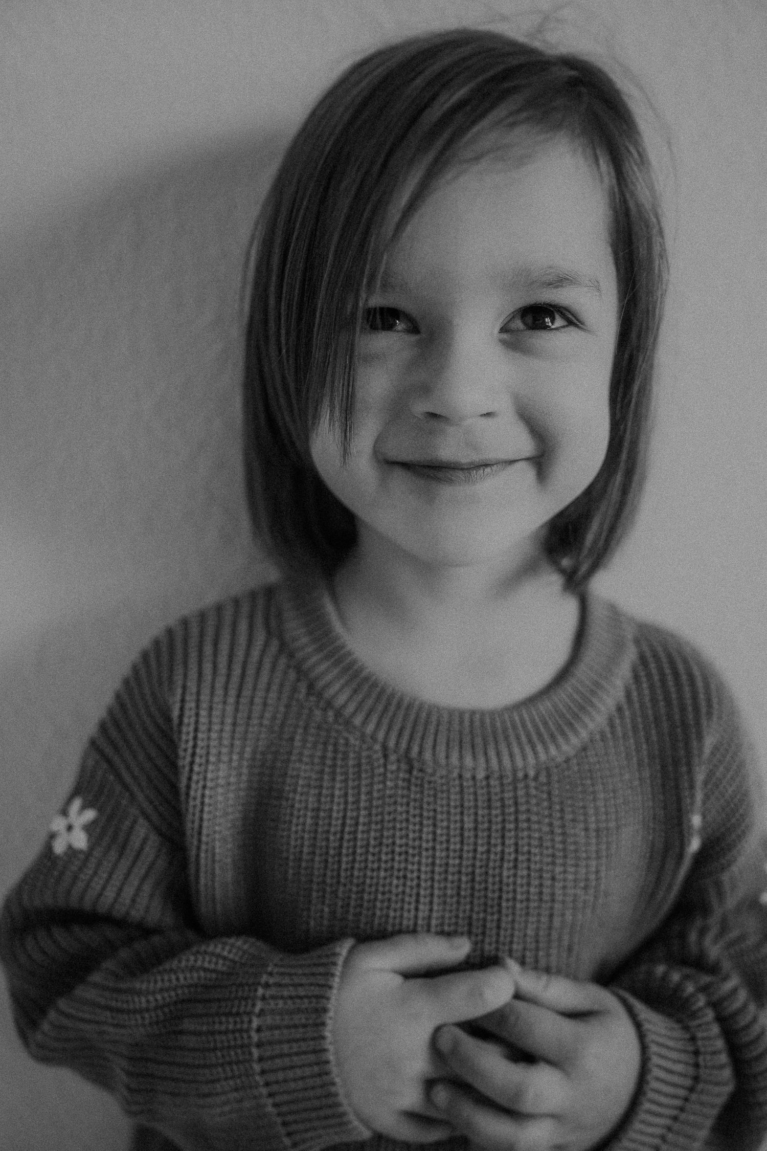 Black and white portrait of a young child in a knit sweater smiling warmly at the camera.