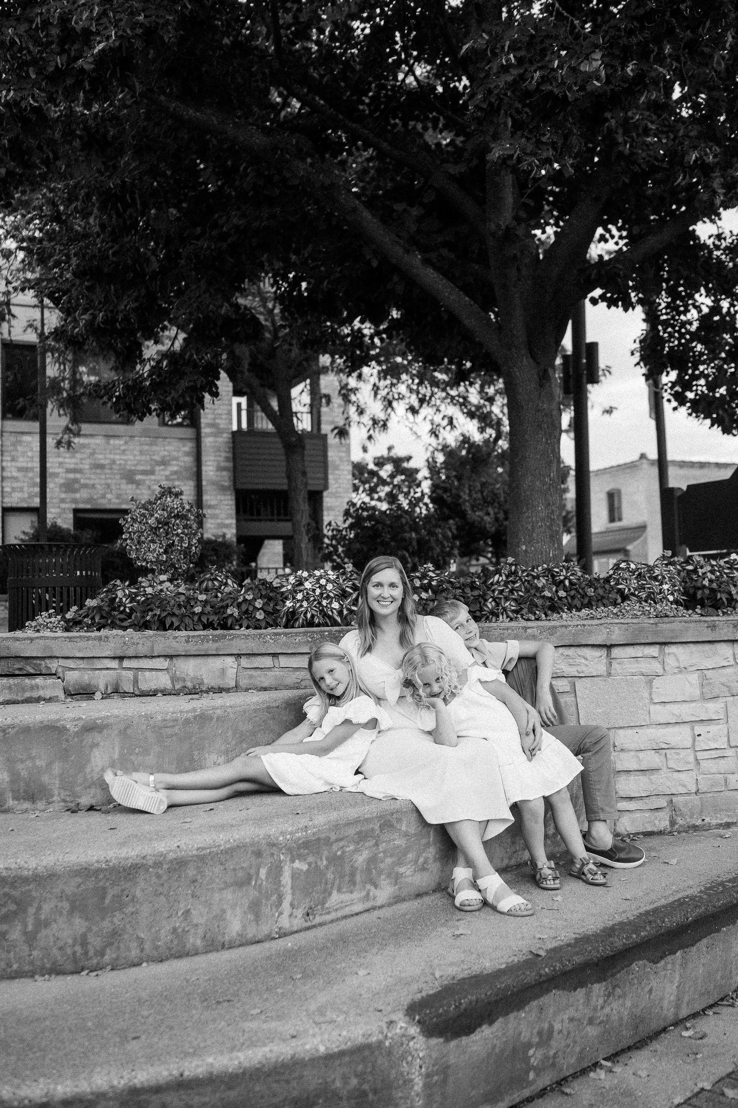 Black and white photo of people relaxing on a stone wall under shady trees.