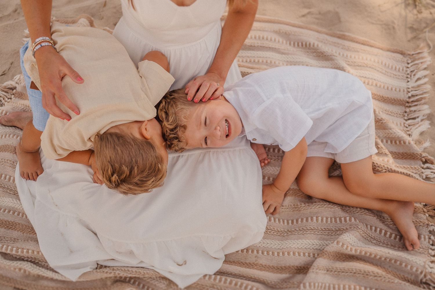 Children resting together on a cozy blanket during a beach photoshoot.