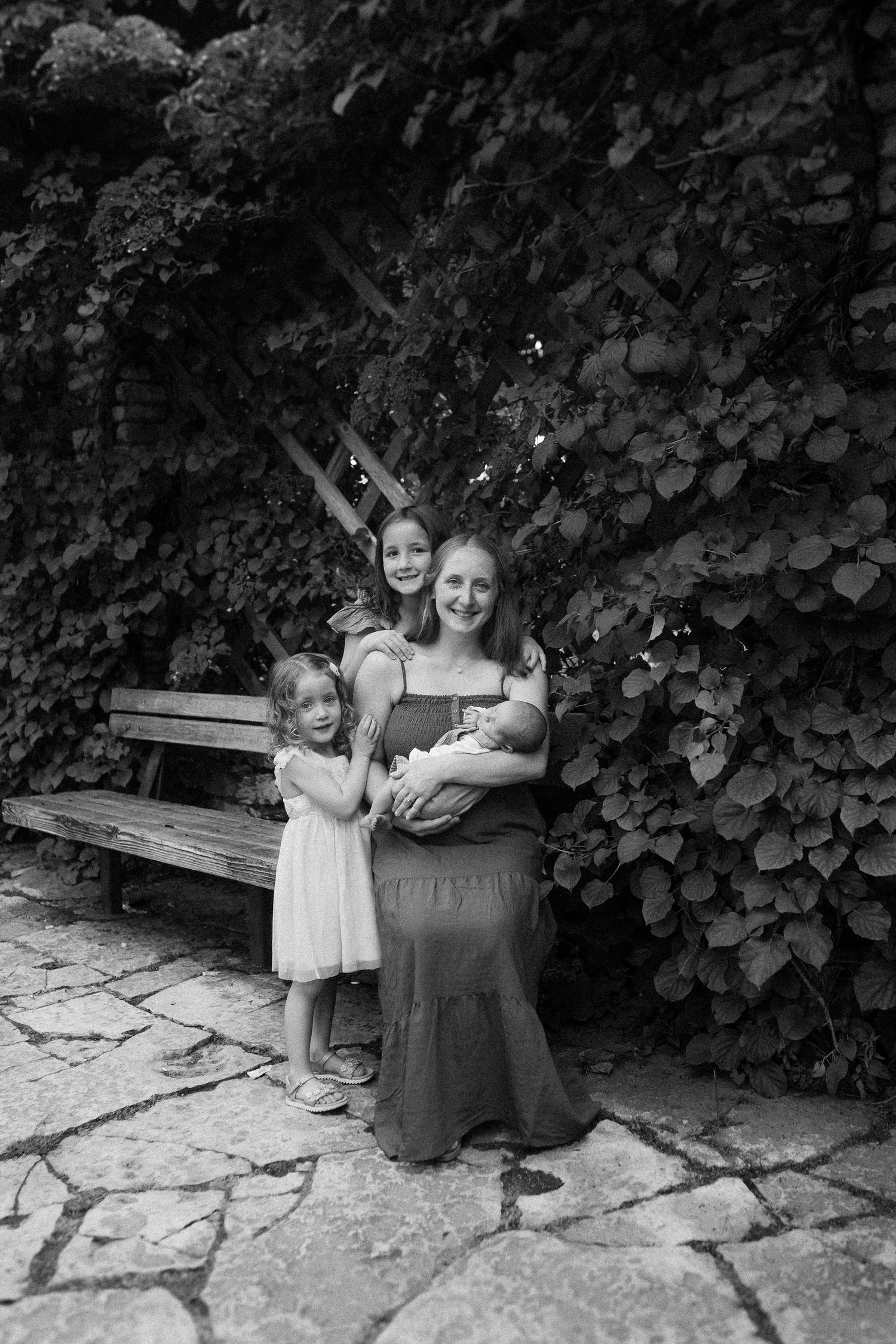 A series of black and white photos showing people sitting together on a stone bench against a leafy wall.