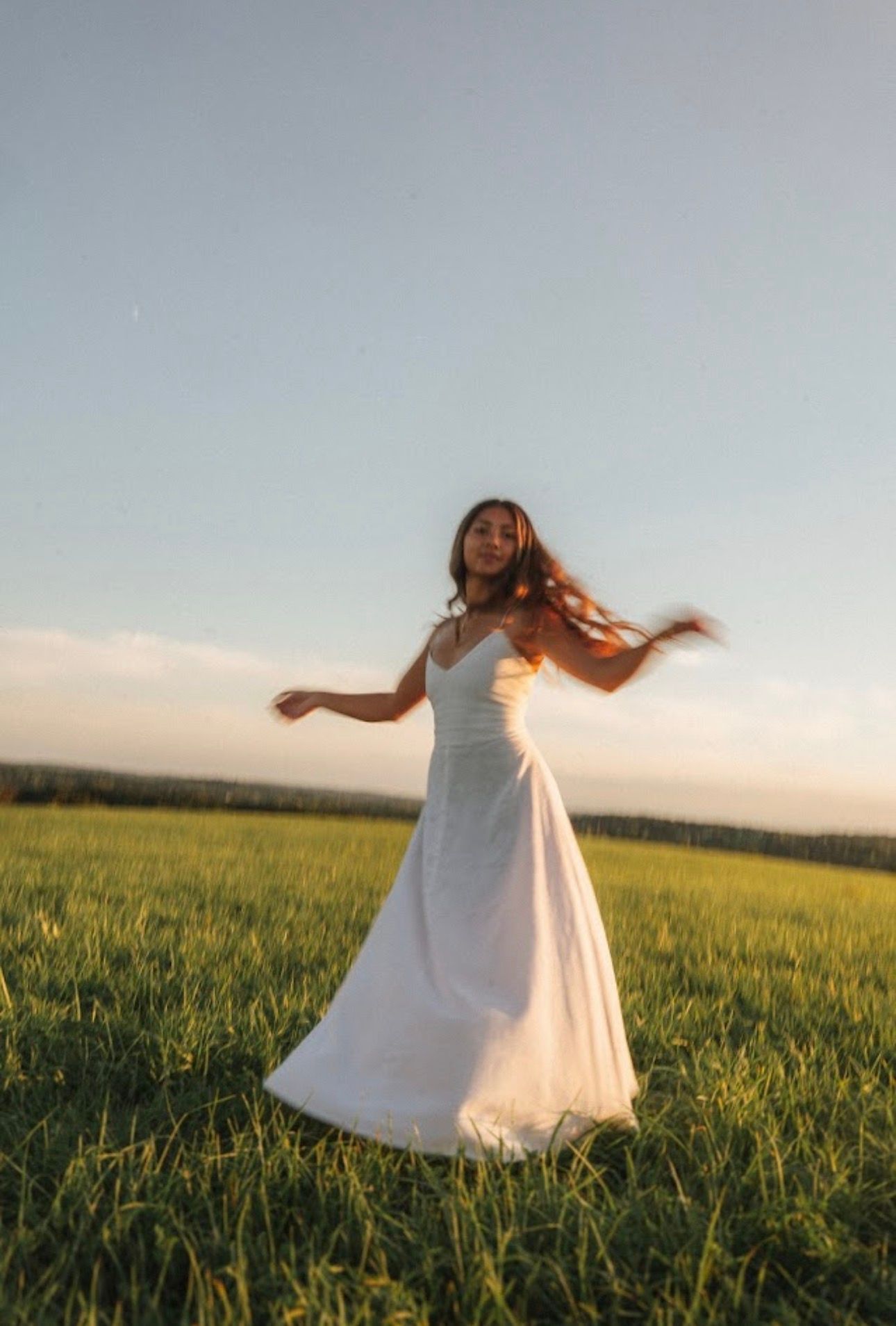 Ethereal scene of person twirling in white dress in open field at sunset.