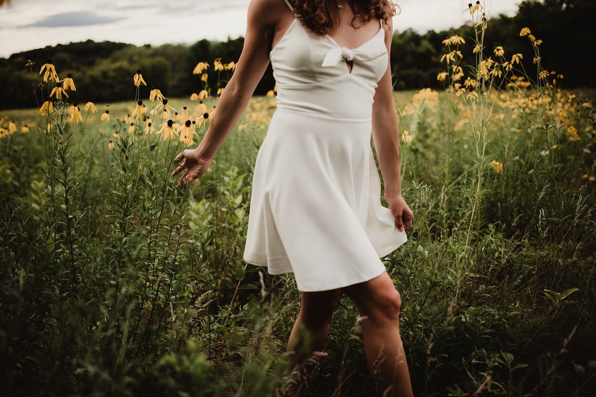 White sundress twirling among yellow wildflowers in golden evening light.
