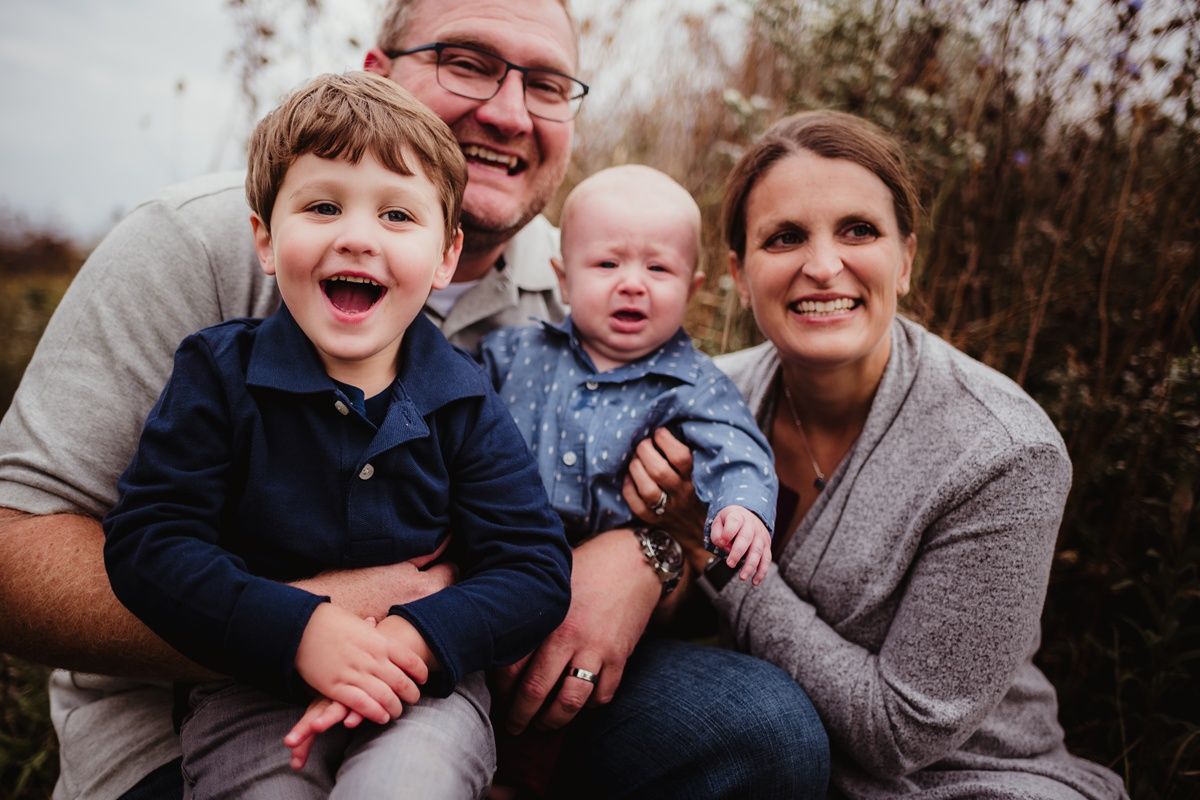 Family of four poses together for outdoor portrait in autumn setting.